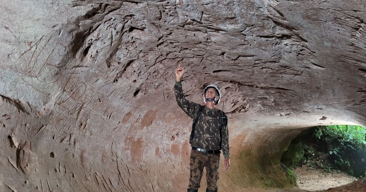 Imagem de uma toca, com um turista dentro, para mostrar as tocas em SC que foram cavadas por animais gigantes 