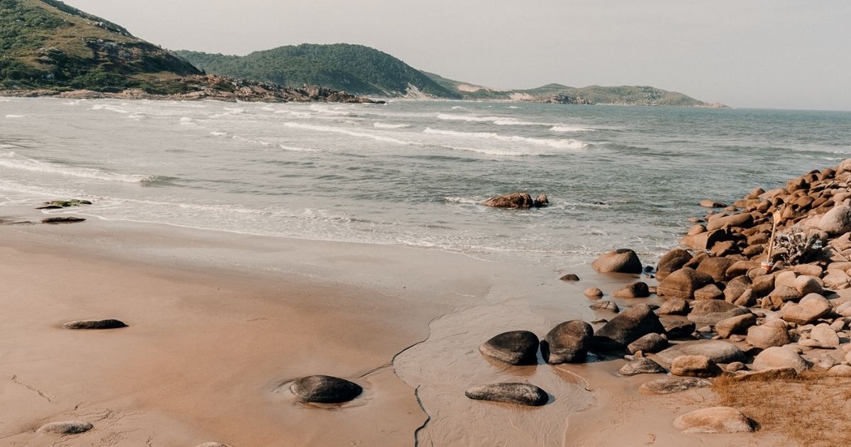 Imagem da Praia da Tereza, com pedras ao redor, mata nativa, costões e um mar cristalino, para mostrar para os leitores como a paisagem se parece