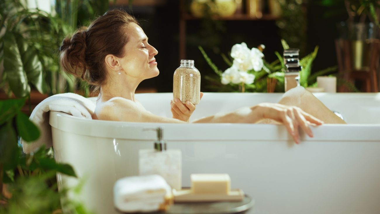 Mulher relaxando em banho de spa com plantas ao redor e relaxamento, promovendo momentos de bem-estar e cuidado pessoal.