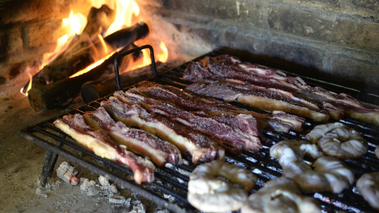 Cortes de carne sendo assados na grelha com fogo de lenha, representando o preparo tradicional de churrasco