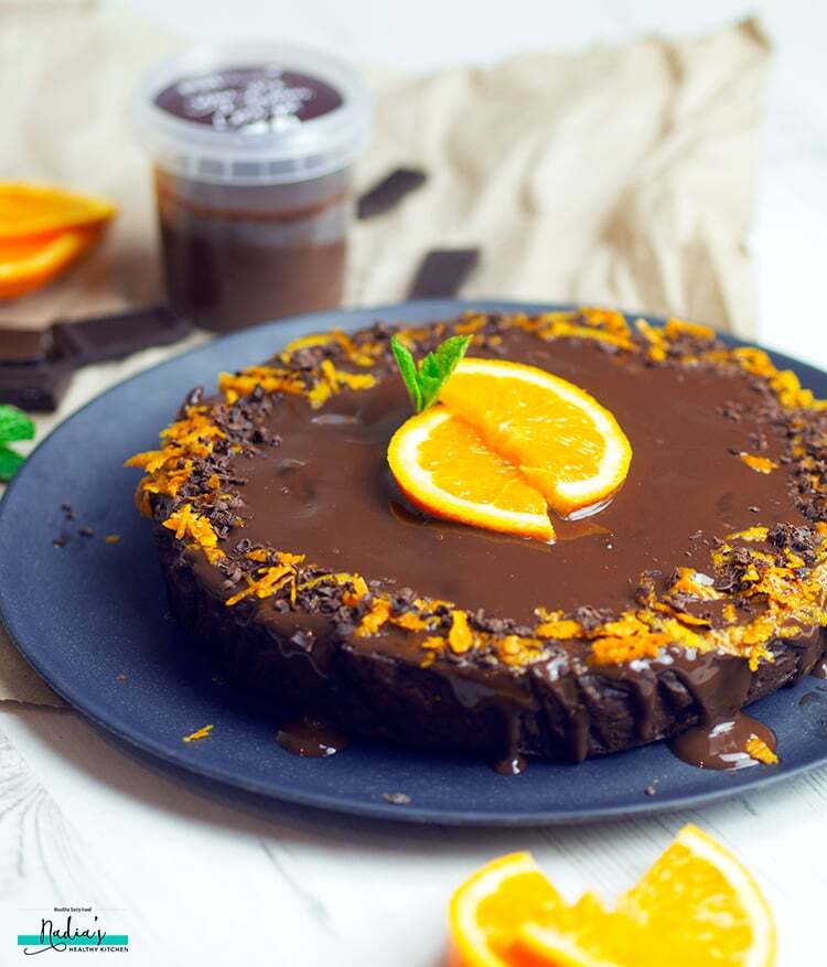 Bolo de laranja com cobertura de chocolate sobre um prato azul. Por cima do bolo, há raspas e pedaços de laranja e pedacinhos de chocolate.