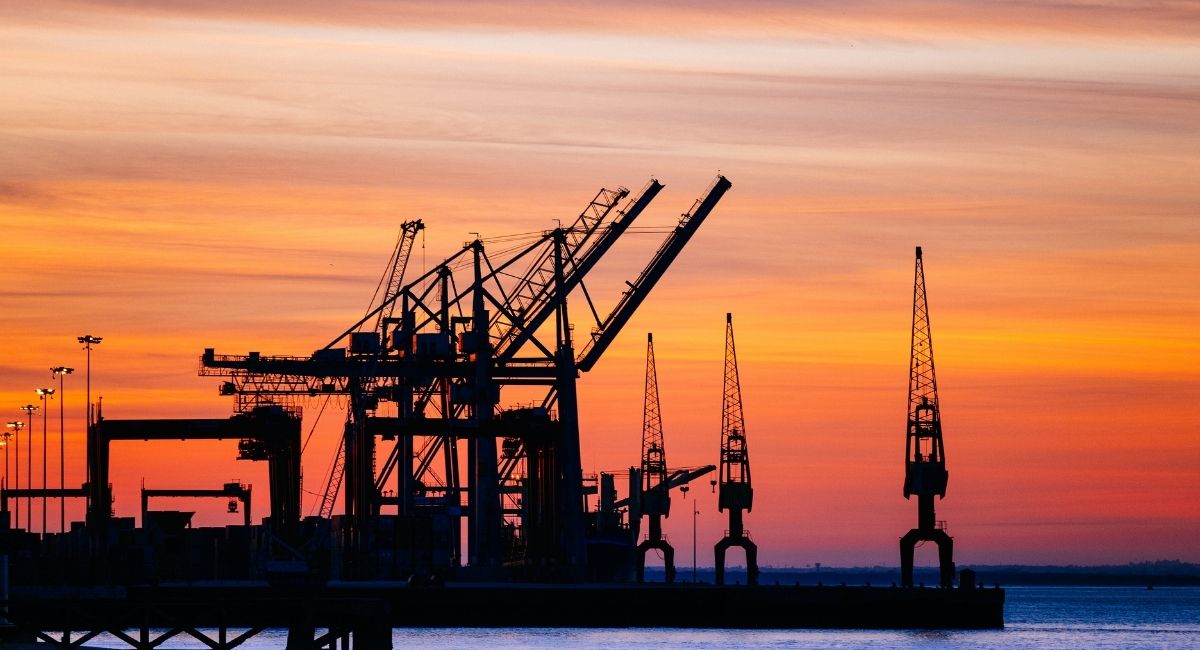 Guindastes portuários em silhueta ao pôr do sol, cenário industrial que mostra o que poucos fariam em ambientes extremos