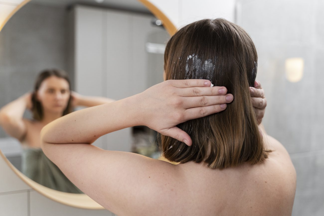 Mulher aplicando creme no cabelo seco, apenas nas pontas, para evitar raiz oleosa e pontas secas 