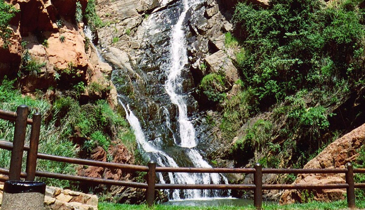 Cachoeira na montanha com rochas e vegetação verde iluminadas pelo sol dourado