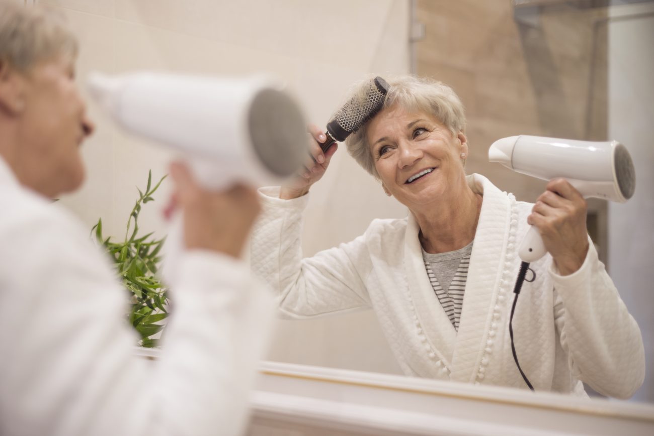 Senhora secando o cabelo com uma escova e um secador 