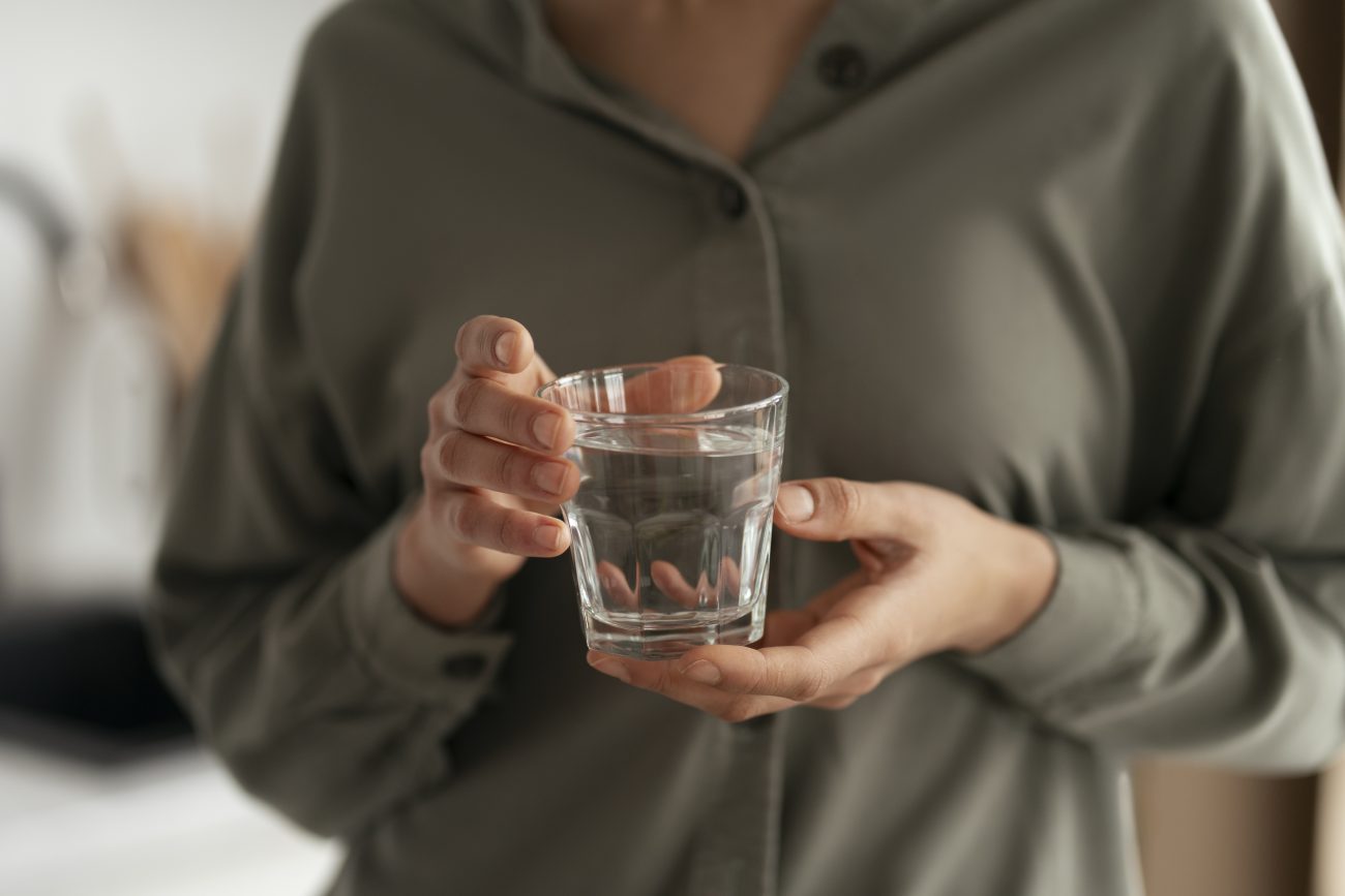 Mulher segurando um copo de água temperatura ambiente para tomar em jejum 