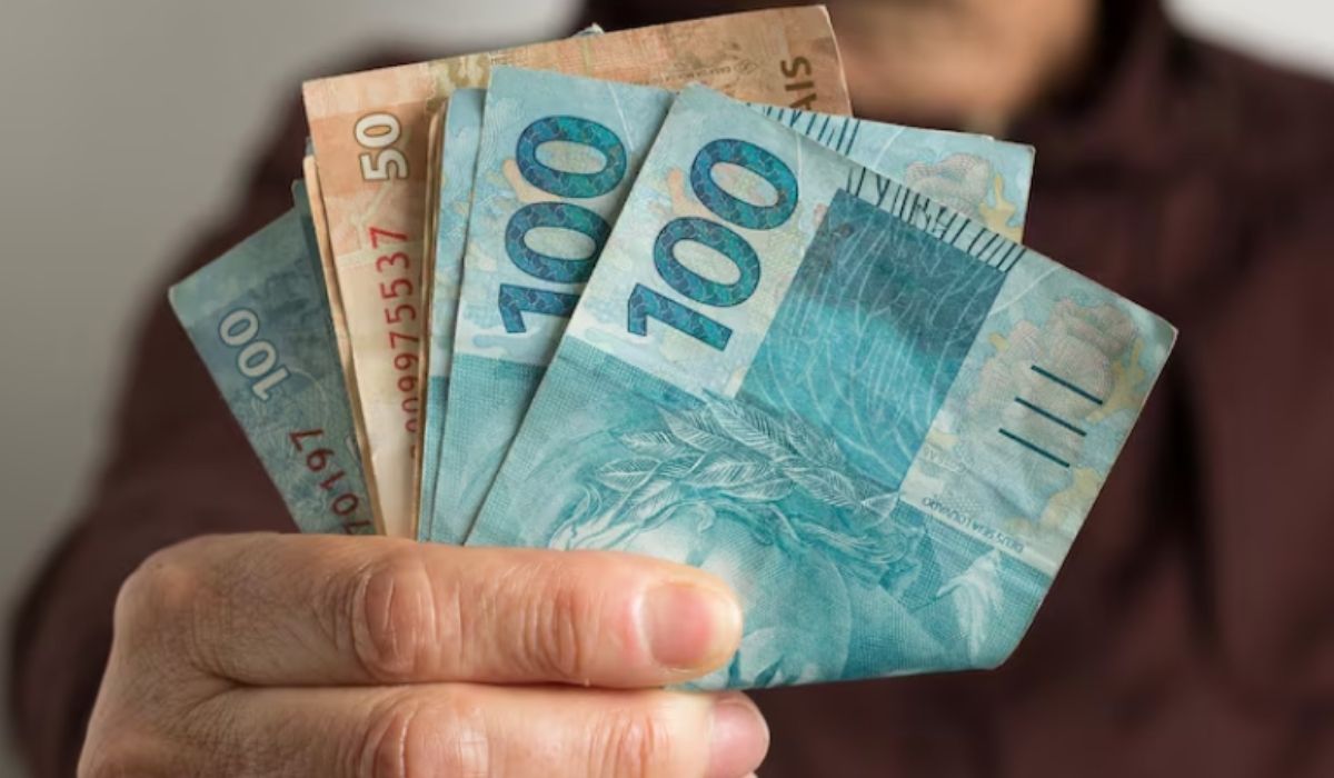 Homem segurando notas de R$ 50 e R$ 100.