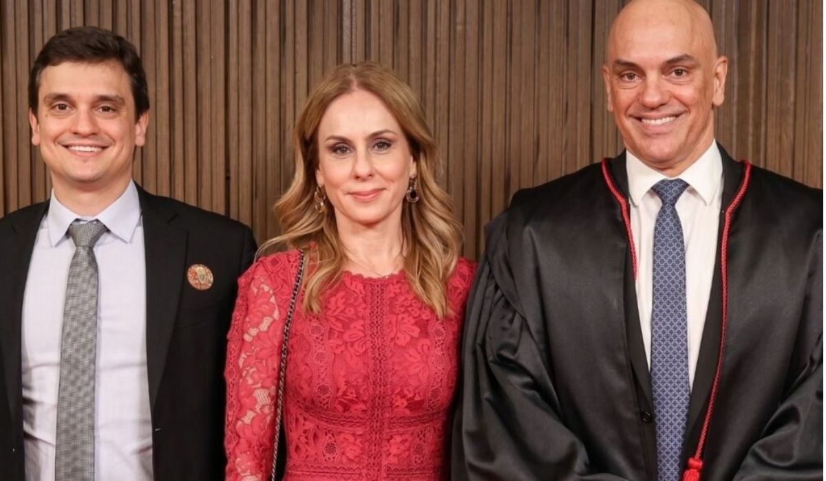 Filho de Moraes posa ao lado de uma mulher e de um ministro durante uma cerimônia oficial.