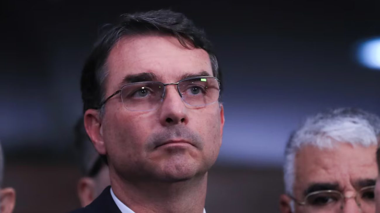 Flávio Bolsonaro (PL) aparece de óculos e expressão séria durante evento político