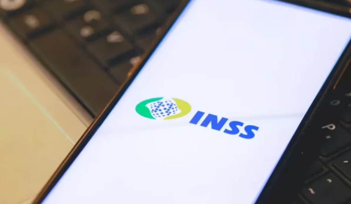 Celular com o logotipo do INSS na tela, apoiado sobre teclado de computador; mulher foi enganada por criminosos que prometeram pagamento de R$ 200 mil