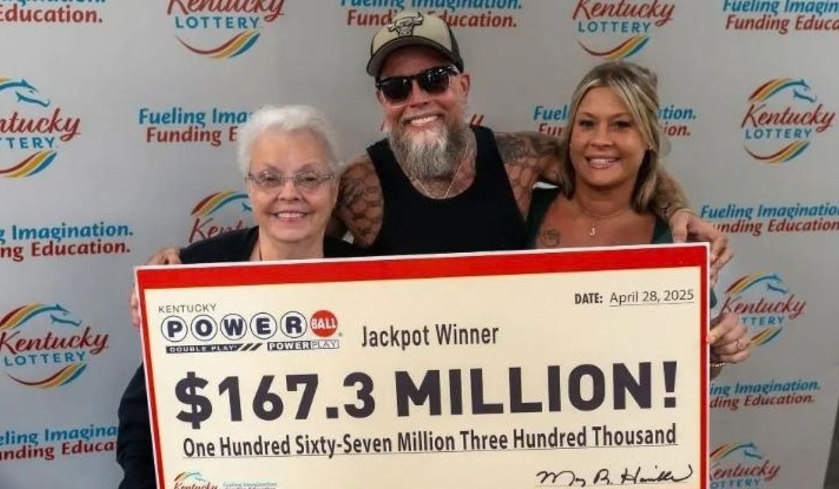 James Farthing posa entre duas mulheres diante de um cheque simbólico de US$ 167,3 milhões da Powerball, em evento da loteria do Kentucky