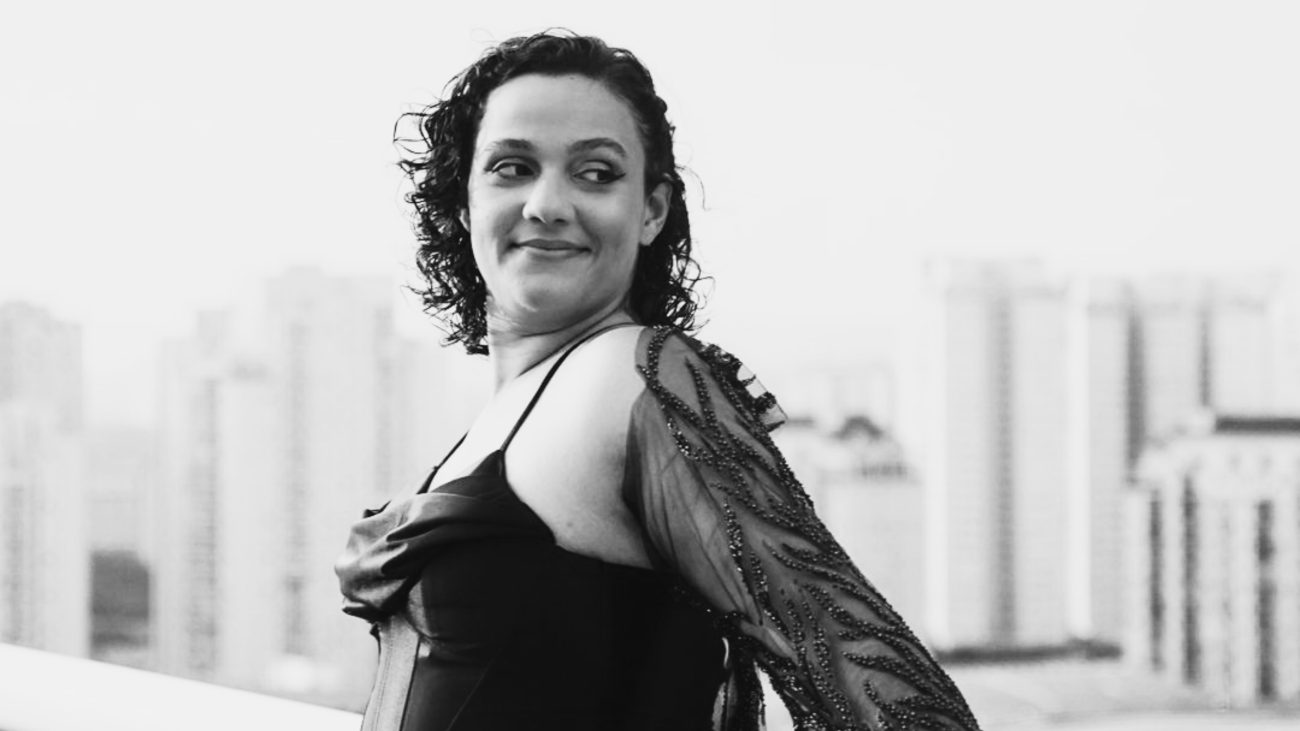 Fernanda Fialho aparece em registro fotográfico em preto e branco, usando um vestido preto com detalhes transparentes e bordados.